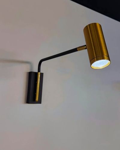 Arandela LED articulada dourada e preta acesa na parede